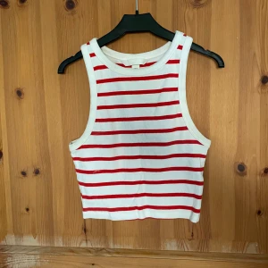 Vit och röd randig linnetopp från H&M - Säljer en snygg vit och röd randig linnetopp från H&M. Toppen är ribbad och croppad, perfekt för sommardagar. Den är ärmlös och har en klassisk rund halsringning.