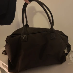 Brun weekend bag med dragkedja - Snygg och rymlig brun axelväska med dragkedja. Perfekt för att bära med sig allt man behöver. Väskan har två handtag och en stilren design.