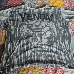 Grå Venom t-shirt från Marvel - Säljer en grå t-shirt med Venom-tryck från Marvel. T-shirten har ett coolt mönster med Venom-motiv och är kortärmad. Perfekt för fans av Marvel-universumet!