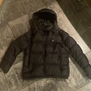Svart dunjacka med huva rhalp lauren - Säljer en svart dunjacka med huva. Jackan har en pufferdesign med dragkedja framtill och långa ärmar. Perfekt för kyliga dagar.
