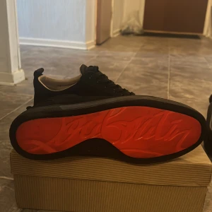 Christen loubitioun  - Snygga svarta sneakers från Christian Louboutin med den ikoniska röda sulan. Skorna har snörning och är tillverkade i skinn. Perfekta för att ge en lyxig touch till din stil. Storlek 44