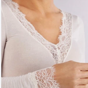 Vit långärmad topp med spetsdetaljer - Elegant vit långärmad topp med v-ringning och vackra spetsdetaljer vid hals och ärmslut. Perfekt för en stilren look.