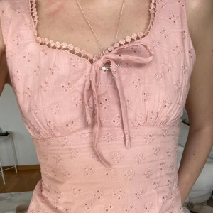 Rosa ärmlös topp med spetsdetaljer - Söt rosa ärmlös topp med spetsdetaljer och knytning framtill.  Costume made i Veitnam aldrig använd! Ny pris 500kr! Toppen har ett broderat mönster och en feminin design som passar perfekt för varma dagar. Dragkedja baktill 