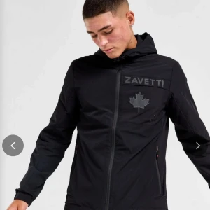 Zavetti Canada jacka - Snygg svart jacka från Zavetti med dragkedja och huva. Jackan har en stilren design med ett diskret märke på bröstet. Perfekt för en cool och avslappnad stil. Byte fungerar också