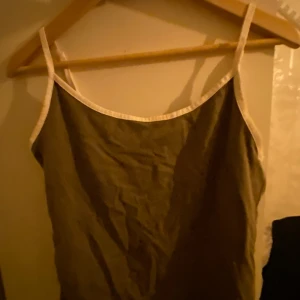 Grön  linnetopp med vita band - Säljer en enkel och stilren grön linnetopp med vita axelband. Perfekt för varma dagar och lätt att matcha med olika outfits.