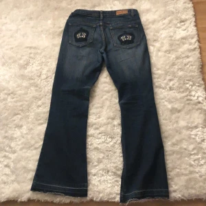 Blå bootcut jeans från S&Y - Snygga blå bootcut jeans från S&Y med broderade detaljer på bakfickorna. Jeansen har en klassisk femficksdesign och en bekväm passform. Perfekta för en avslappnad stil. Mått står på sista sidan jeansen är uppsprättade längt ut men går att sy igen om de behövs kortas ner. 