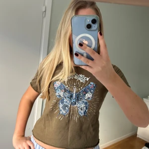 Olivgrön t-shirt med fjärilstryck - Snygg olivgrön t-shirt från Zadig med ett stort fjärilstryck i blått och grått på framsidan. T-shirten har avklippta kanter vilket gör den väldigt snygg