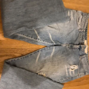 Blå jeans med slitningar - Snygga blå jeans med slitningar på låren och knäna. De har en klassisk femficksdesign och en bekväm passform. Perfekta för en avslappnad stil.