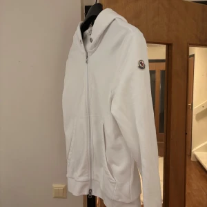 Moncler kofta - Säljer en stilren vit kofta från Moncler med dragkedja och huva. Inte använd så mycket 