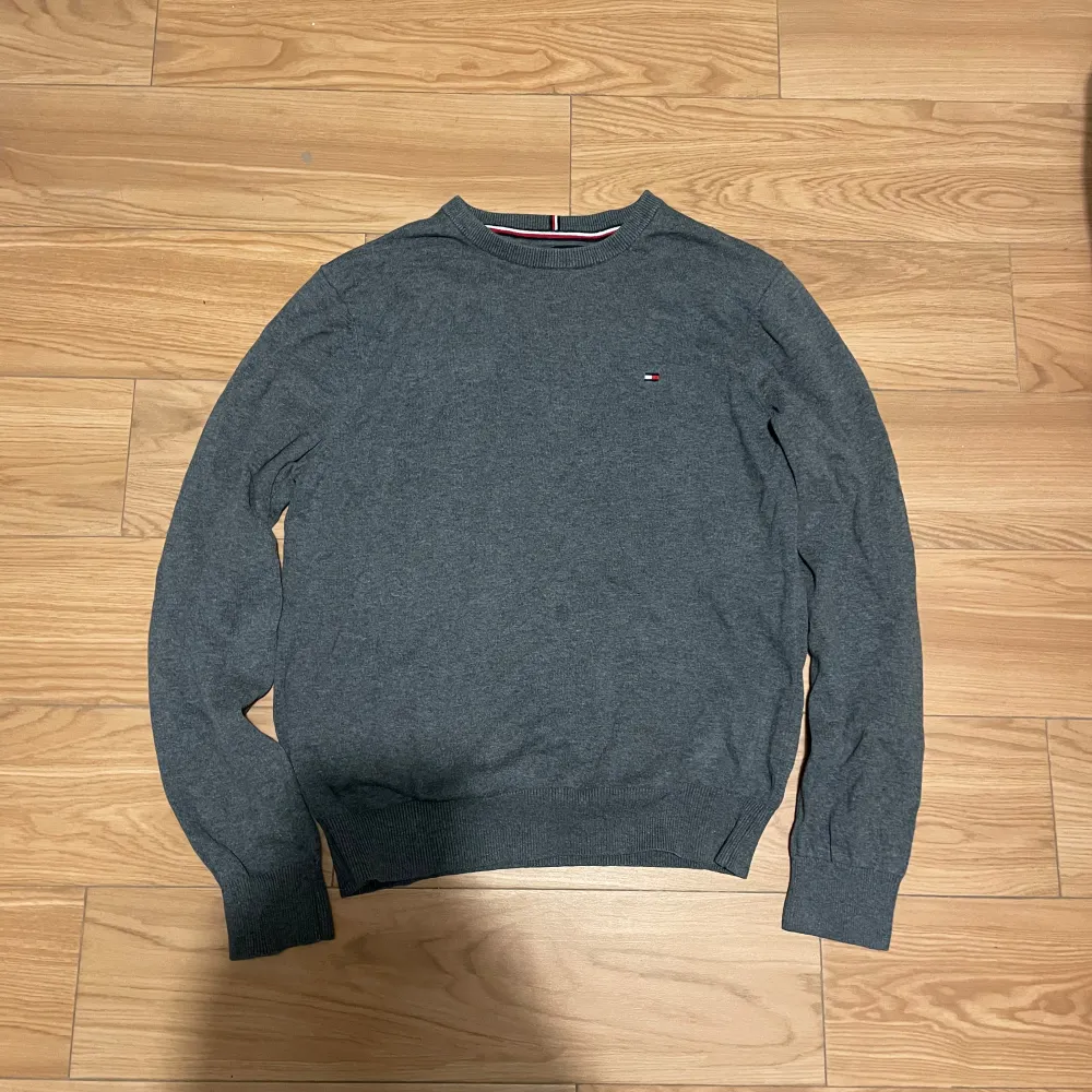 Säljer en stilren grå tröja från Tommy Hilfiger med deras ikoniska logga på bröstet. Tröjan har långa ärmar och ribbade muddar vid ärmslut och nederkant. Perfekt för en avslappnad och snygg look.. Neuletakit & Villapaidat.