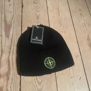 Svart mössa från Stone Island - Snygg svart mössa från Stone Island med broderad logga framtill. Säljs oanvänd och prislappen sitter fortfarande på, säljer för ungefär som ny pris men ett snäpp billigare då den ändå räknas som begagnat. kan tänka mig gå ner om affären sker snabbt och smidigt. pm för frågor:)