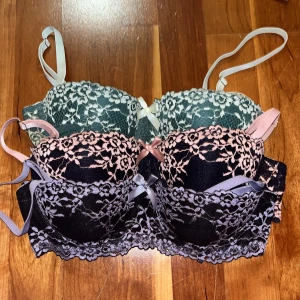 Färgglada spets-bh:ar med rosett - Säljer ett set av tre bh:ar i olika färger med vacker spets och små rosetter framtill. Färgerna är grön, rosa och lila. Bh:arna har justerbara axelband och en bekväm passform. Avtagbara axelband! 