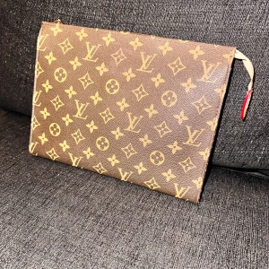 Brun monogram kuvertväska - Snygg brun kuvertväska med det klassiska monogrammet. Väskan har en dragkedja upptill och är perfekt för att hålla dina viktigaste saker samlade. Den är tillverkad i slitstarkt skinnmaterial och har en elegant design som passar till många tillfällen.