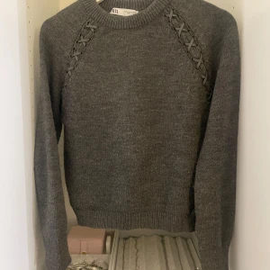 Grå stickad tröja från Zara - Säljer en snygg grå stickad tröja från Zara med unika snörningsdetaljer längs ärmarna. Väldigt bra skick och super skön