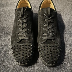 Svarta sneakers med nitar - Snygga svarta sneakers i mocka från Christian Louboutin med coola nitar på tån och den ikoniska röda sulan. Skorna har snörning och en stilren design som sticker ut. Skick 9/10 samt nypris på 10 tusen kronor. Pris kan även diskuteras👍