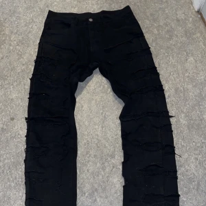 Svarta jeans med slitningar - Snygga svarta jeans med slitningar längs benen. De har en knapp och dragkedja framtill. Perfekta för en edgy looke. USA klädstil