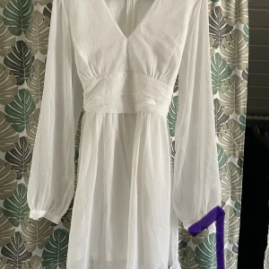Vit långärmad klänning från bubberoom  - Elegant vit klänning med långa ärmar och v-ringad hals. Den har en knytning i midjan som ger en fin siluett. Perfekt för vår och sommar.