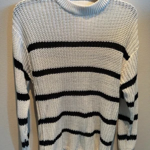 Vit och svart randig stickad tröja - Säljer en snygg vit stickad tröja med svarta ränder. Tröjan har en klassisk rund hals och långa ärmar, perfekt för kyligare dagar. Den är både stilren och bekväm.