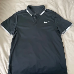 Pikétröja från Nike - Svart pikétröja från Nike med Dri-FIT-teknologi. Perfekt för en sportig look eller en avslappnad dag.