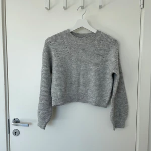 Grå stickad tröja från KappAhl - Säljer en mysig grå croppad stickad tröja från KappAhl. Tröjan har en ribbad rund hals och långa ärmar. Lite nopprig, men annars i fint skick! I storlek 146/152. 
