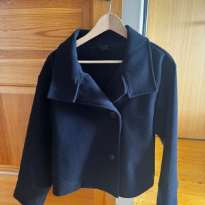 Mörkblå kappa från Gina - Snygg blå kappa med knappar framtill och bred krage. Perfekt för kyligare dagar och ger en stilren look. Passar bra till både jeans ock klänningar. Använd ett par gånger och köpt på Gina