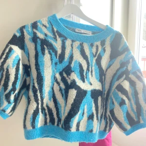Mönstrad tröja från Zara - Säljer en cool tröja från Zara med ett iögonfallande mönster i blått, svart och vitt. Tröjan har en croppad passform och trekvartsärmar, perfekt för en trendig look. Den är tillverkad i ett mjukt material som känns skönt mot huden.