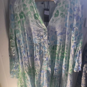 Leopard Mönstrad klänning från Qnuz - Säljer en färgglad leopard  klänning från Qnuz med ett  mönster i grönt och blått. Klänningen har långa ärmar och knappar framtill. Perfekt för en somrig look!