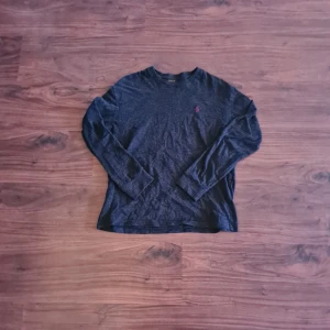 Mörkgrå tröja - Säljer en stilren mörkblå långärmad tröja från Polo Ralph Lauren. Tröjan har en liten broderad logotyp i rött på bröstet och är tillverkad i ett mjukt material.