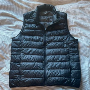 Svart dunväst  - Säljer en stilren svart dunväst från Uniqlo. Västen är ultralätt och har en dragkedja framtill. Perfekt för lager-på-lager under kyliga dagar eller en varm sommar kväll. Passar även M. Mycket bra skick, förutom ett litet märke (bild 3) som inte syns vid användning. Pris går att diskutera vid snabb affär. 