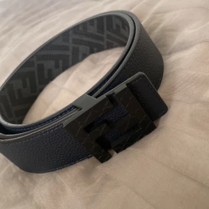 Blått bälte från Fendi - Snyggt blått bälte från Fendi med en stilren svart spänne. Bältet har en texturerad yta och är tillverkat i Italien. Perfekt för att ge en lyxig touch till din outfit. Storlek 100/40