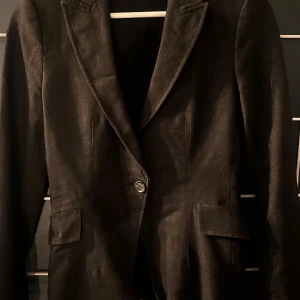 Svart kavaj från Zara Basic - Elegant svart kavaj från Zara Basic med klassisk design. Kavajen har långa ärmar och stängs med en knapp framtill. Perfekt för en stilren look.