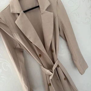Beige trenchcoat med knytbälte - Beige trenchcoat med knytbälte och knappar framtill. Perfekt inför våren 🤎