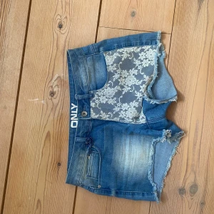 Jeansshorts med spetsdetaljer från Only - Snygga jeansshorts från Only med unika spetsdetaljer på framsidan. De har en fransig kant och en klassisk blå jeansfärg. Perfekta för en somrig look!