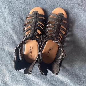 Svarta sandaler med remmar - Snygga svarta sandaler med flera remmar och öppen tå. Perfekta för sommarens varma dagar. De har en stilren design med små dekorativa detaljer på remmarna.