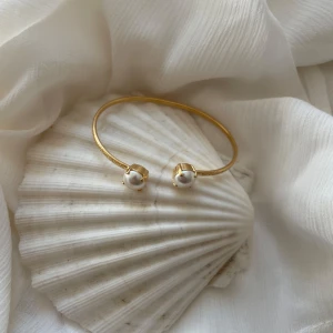 Guldarmband med pärlor - Elegant guldarmband med två vita pärlor. Perfekt för att ge en sofistikerad touch till din stil. Armbandet har en enkel och stilren design som passar till många tillfällen.