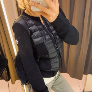 Svart  Moncler cardigan  - Snygg svart dunväst från Moncler med dragkedja och två praktiska fickor framtill. Västen har en quiltad design och är perfekt för lager-på-lager-stil. Den har en rund halsringning och Moncler-logga på bröstet.