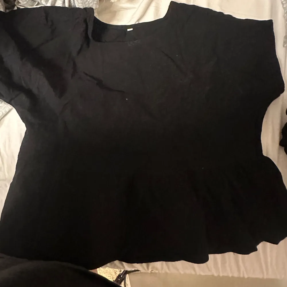 Säljer en svart kortärmad topp i ett mjukt material. Perfekt för en avslappnad stil. Toppen har en rund halsringning och en lös passform.. Yläosat.