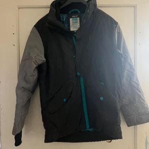 Svart och grå jacka från WA Action Sports - Säljer en svart och grå jacka från WA Action Sports med turkosa detaljer. Jackan har långa ärmar och en dragkedja framtill. Perfekt för utomhusaktiviteter med TCS Water 3000-teknologi för extra skydd mot väder och vind.