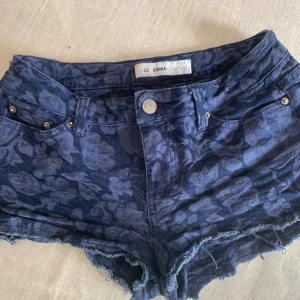 Blå blommiga lågmidjade  jeansshorts från Emma Denim - Säljer ett par snygga blå jeansshorts från Emma Denim med blommigt mönster. Shortsen har en lågmidja med fransiga kanter och en knapp framtill. Perfekta för en avslappnad sommarlook!