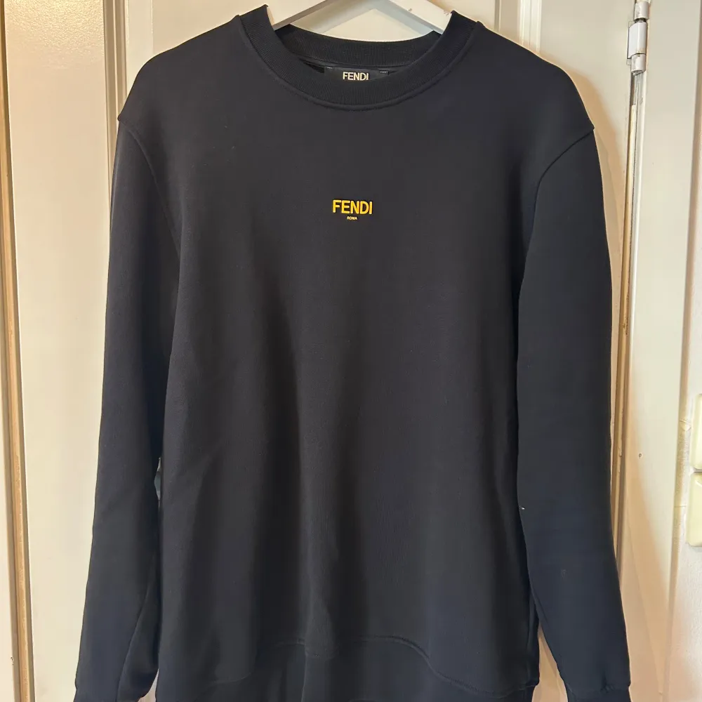 Snygg svart tröja från Fendi med gul logga på bröstet. Tröjan har en klassisk rund hals och långa ärmar. Perfekt för en stilren look.. Neuletakit & Villapaidat.