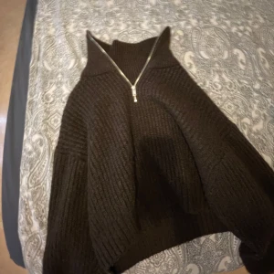 Brun stickad tröja med dragkedja - Säljer en mysig brun stickad tröja med hög krage och dragkedja framtill. Perfekt för kyliga dagar med sin ribbade design och långa ärmar. En stilren och bekväm tröja för alla tillfällen. Väldigt varm och skön.