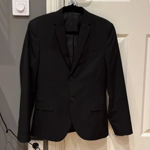 Svart kostym med kavaj och byxor - ‼️BILLIGARE VID SNABB AFFÄR‼️Elegant svart kostym med en stilren kavaj och matchande byxor. Kavajen har två knappar och klassiska fickor, perfekt för formella tillfällen och bal. Byxorna har en rak passform och bälteshällor.