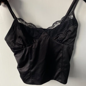 Svart linne från Bik Bok - Snygg svart linne från Bik Bok med spetsdetaljer vid halsringningen. Toppen har smala axelband och en omlott-design framtill. Perfekt för en stilren look. Skicka gärna prisförslag!🩷