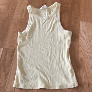 Gul ribbad linnetopp - Säljer en ljusgul ribbad linnetopp. Perfekt för varma dagar med sin ärmlösa design och mjuka material. Enkel och stilren, passar till det mesta i garderoben.