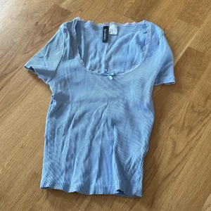 Blå randig topp från H&M - Säljer en söt blå randig topp från Gina Tricot. Toppen har korta ärmar och en rundad halsringning med en liten volangdetalj. Perfekt för en avslappnad stil.