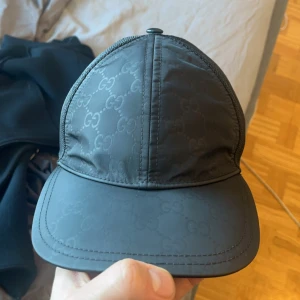 Svart keps från Gucci - Snygg svart keps från Gucci med diskret mönster och justerbar baksida. Perfekt för en stilren look med nätpaneler för ventilation.