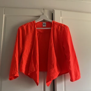 Orange/korall färgad tunn  kofta från Vero Moda - Snygg orange/korall tunn kofta från Vero Moda i storlek S. Kavajen har en öppen design utan knappar och trekvartsärmar, vilket ger en avslappnad och modern look. Perfekt för att liva upp vilken outfit som helst.