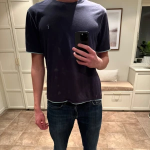 Mörkblå t-shirt från Yves Saint Laurent - Snygg mörkblå t-shirt från Yves Saint Laurent med ett diskret broderat YSL-logotyp på bröstet. T-shirten har en klassisk passform och är tillverkad i mjuk bomull. Perfekt för en stilren look Sitter som M.