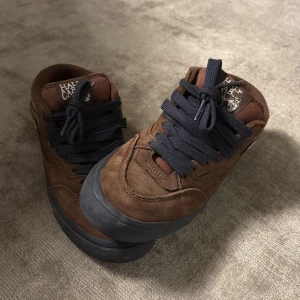 Bruna Vans Half Cab sneakers - Snygga bruna Vans Half Cab sneakers i mocka med mörkblåa snören och en robust svart sula. Perfekta för skateboarding eller en avslappnad stil. Märkesdetaljer på plösen och insidan ger en cool touch.