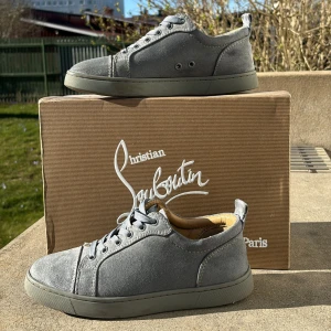 Grå sneakers från Christian Louboutin - Snygga grå sneakers i mocka från Christian Louboutin med den ikoniska röda sulan. Skorna har snörning och en stilren design som passar perfekt för en trendig look.